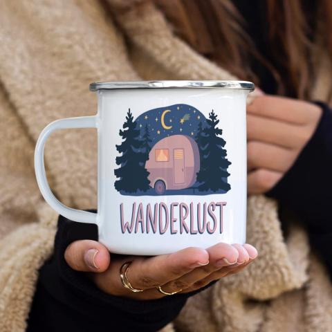 Mug being held that says Wanderlust, with a camper and trees on it.